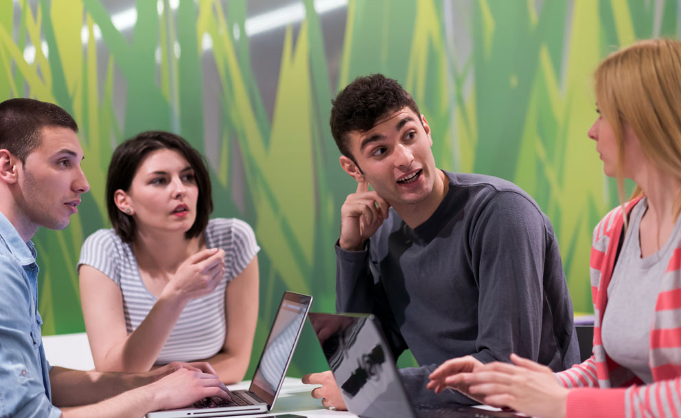 Mixed group of students sat at a table, have a discussion